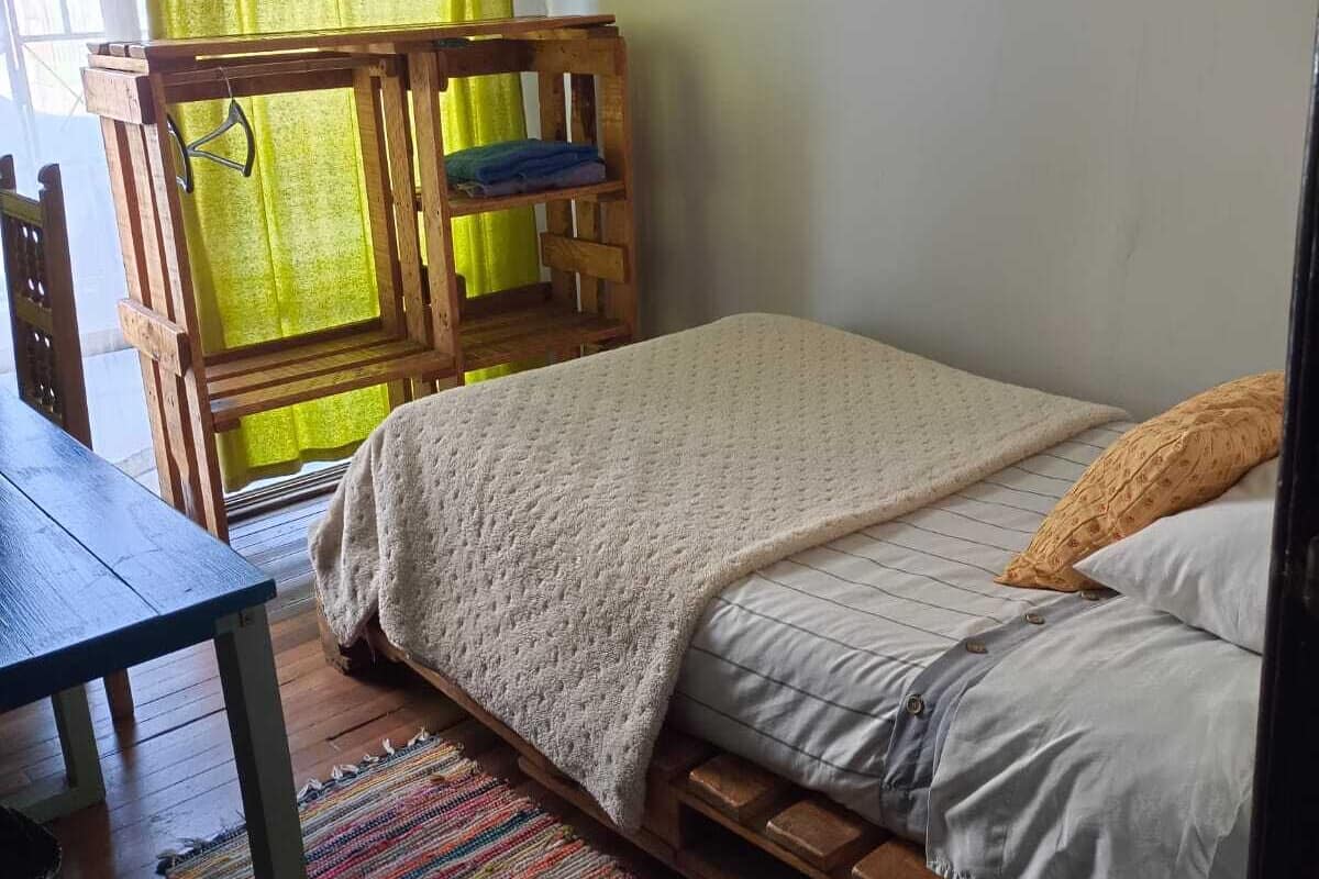 Una habitació acollidora amb un llit de fusta, una taula de fusta petita i una manta de llana colorida.