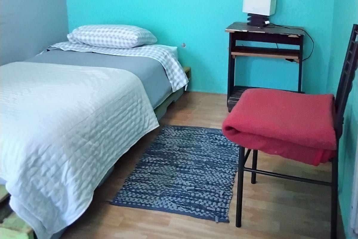 Habitació petita i ordenada amb un llit, una taula i una cadira.