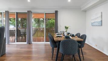 A dining area with a table set for four, chairs, a view through a glass door to an outdoor deck, and a painting on the wall.
