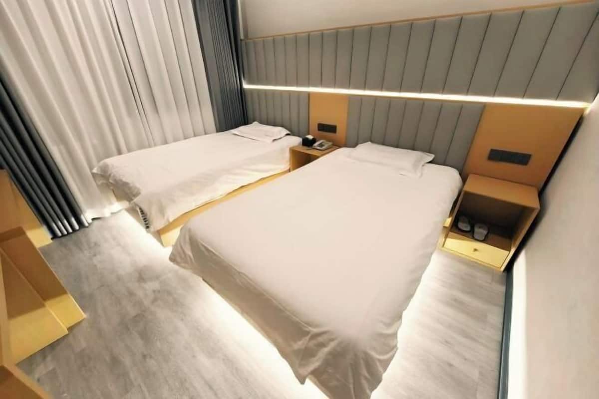 A hotel room with two beds, a bedside table with a phone, and a headboard with built-in lighting.