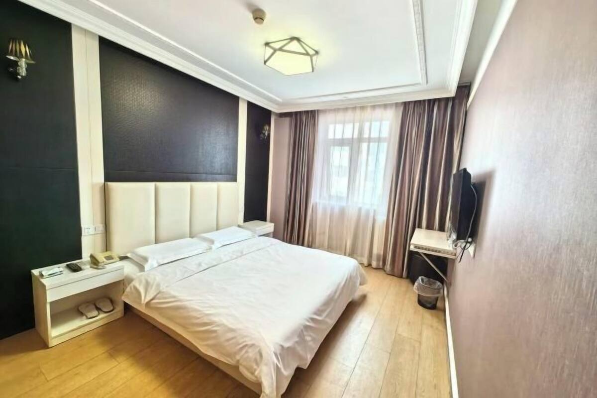 A hotel room with a bed, bedside table, lamp, and a wall-mounted TV.
