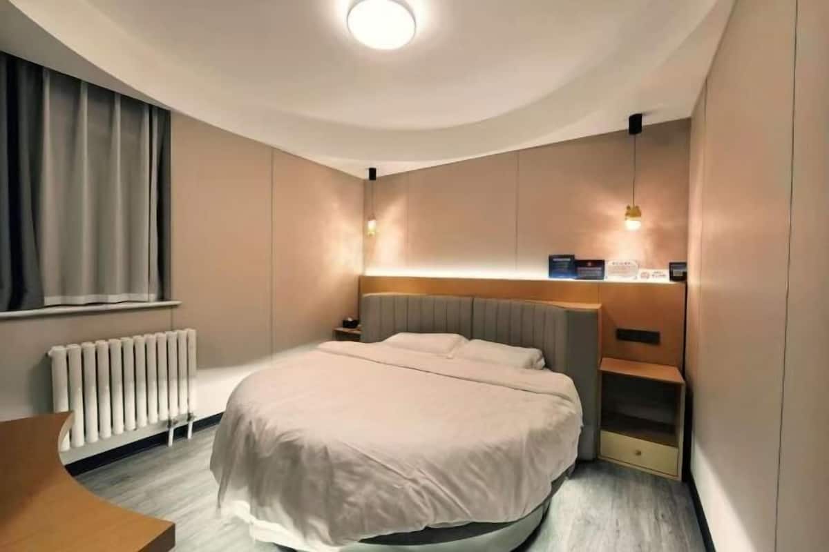 A modern hotel room with a bed, bedside table, lamp, and a view of the city.