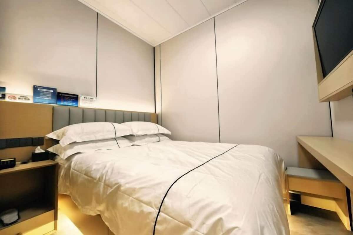 A modern hotel room with a bed, bedside table, and a flat-screen TV mounted on the wall.