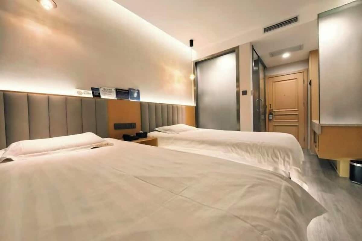 A hotel room with two beds, a bedside table, a nightstand, a wardrobe, and a bathroom door.