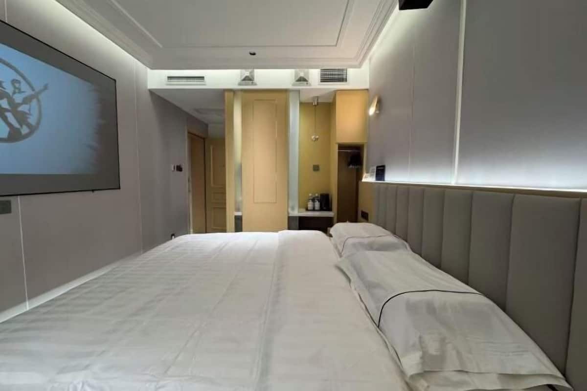 A hotel room with a large bed, a TV screen, and a door leading to a bathroom.