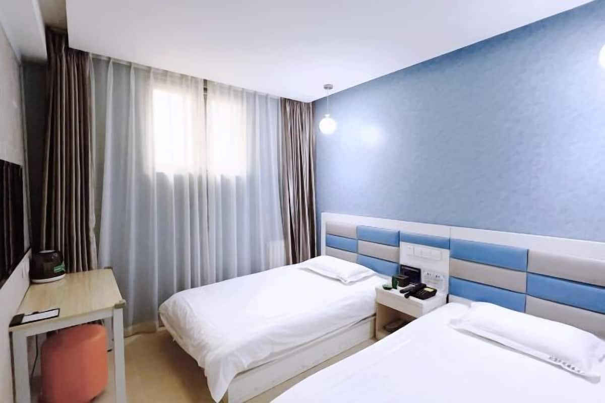 A hotel room with two beds, a desk, a chair, and a window with curtains.