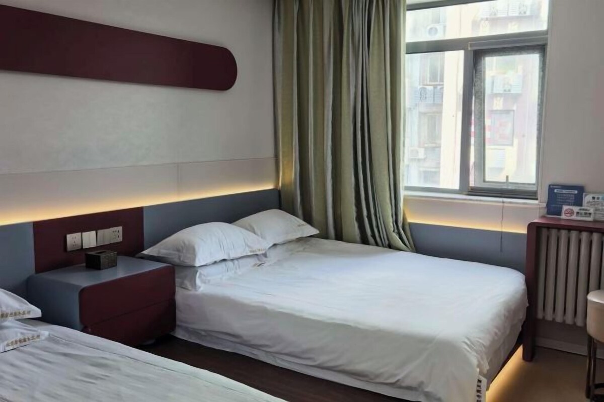 Una habitación de hotel con cama, mesita de noche y ventana con cortinas.