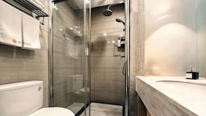 Un baño moderno con ducha de vidrio, inodoro blanco y encimera de mármol.