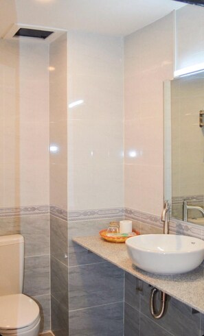 A bathroom with a white sink, a toilet, and a mirror. - Apollo Vientiane Hotel (Vientiane)