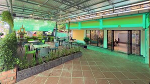 An outdoor patio area with green chairs and tables, a brick floor, and a green wall with a decorative pattern. - Apollo Vientiane Hotel (Vientiane)