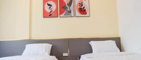 Habitación de hotel con dos camas, una mesita de noche y tres cuadros abstractos en la pared.