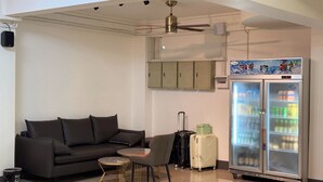 A modern room with a sofa, a small round table, a chair, a refrigerator, and a ceiling fan. - Apollo Vientiane Hotel (Vientiane)