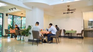 A spacious dining area with multiple tables and chairs, a ceiling fan, and a large window with decorative glass. - Apollo Vientiane Hotel (Vientiane)