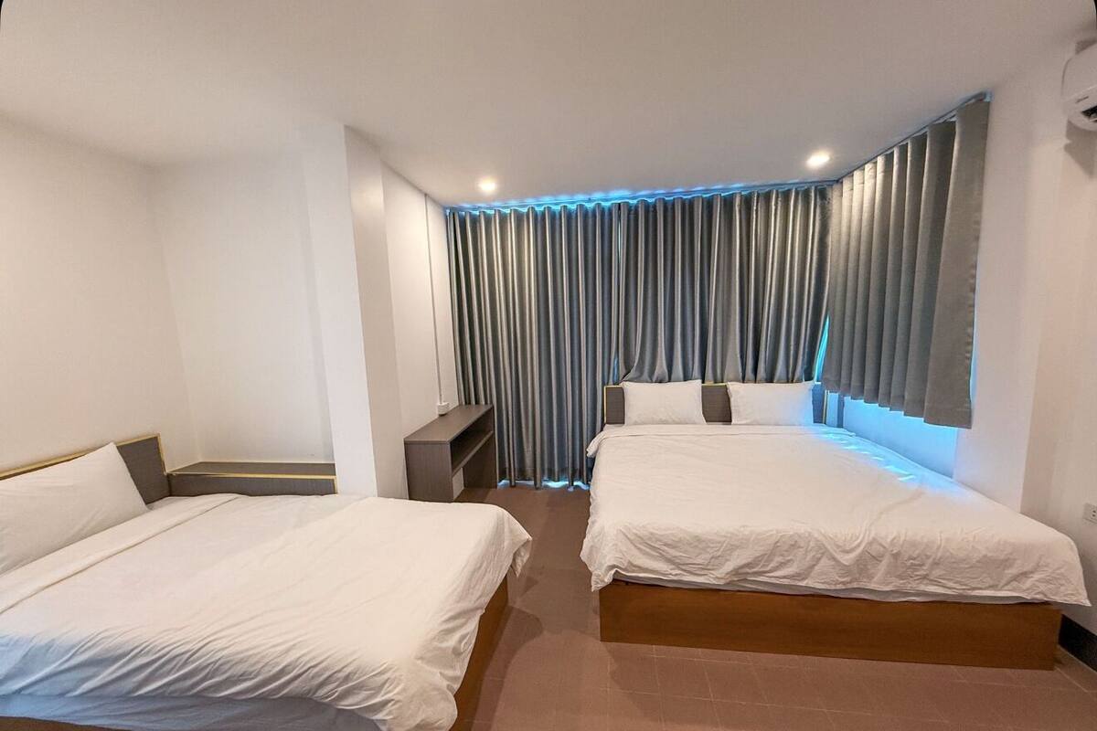A hotel room with two single beds, a small desk, and a large window with curtains.