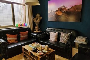 A living room with a black leather sofa, a wooden coffee table, and a painting on the wall.