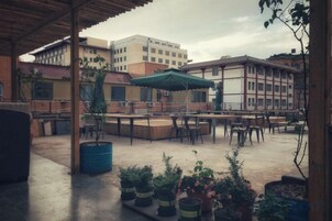 Un patio al aire libre con mesas y sillas, plantas en macetas y un edificio al fondo.