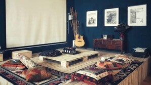 A cozy living room with a large window, a guitar, a wooden coffee table, and a sofa with patterned cushions. - up north hostel (Dunhuang)