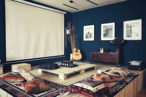 A cozy living room with a large window, a guitar, a wooden coffee table, and a sofa with patterned cushions.