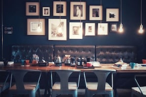 A restaurant with a dark wall, framed pictures, a long wooden table, and cushioned chairs.