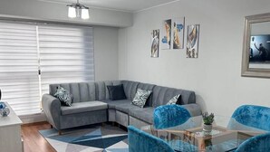 A modern living room with a gray sectional sofa, a glass coffee table, and blue chairs.