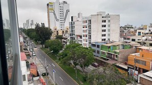 A cityscape with multi-story buildings, a wide road, and greenery.