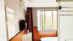 Ein Hotelzimmer mit Bett, Schreibtisch, Stuhl, einem Fenster mit Vorhängen und einer Wand-Klimaanlage.