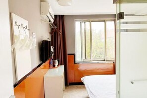 Une chambre d’hôtel équipée d’un lit, d’un bureau, d’une chaise, d’une fenêtre avec des rideaux et d’un climatiseur fixé au mur.