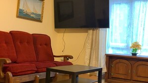 A living room with a red sofa, a wooden cabinet, and a television mounted on the wall. - Room-king Bed With Shared Bath (Dublin)