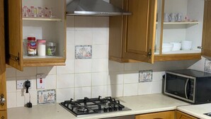 A kitchen with wooden cabinets, a gas stove, a microwave, and a tiled backsplash. - Room-king Bed With Shared Bath (Dublin)