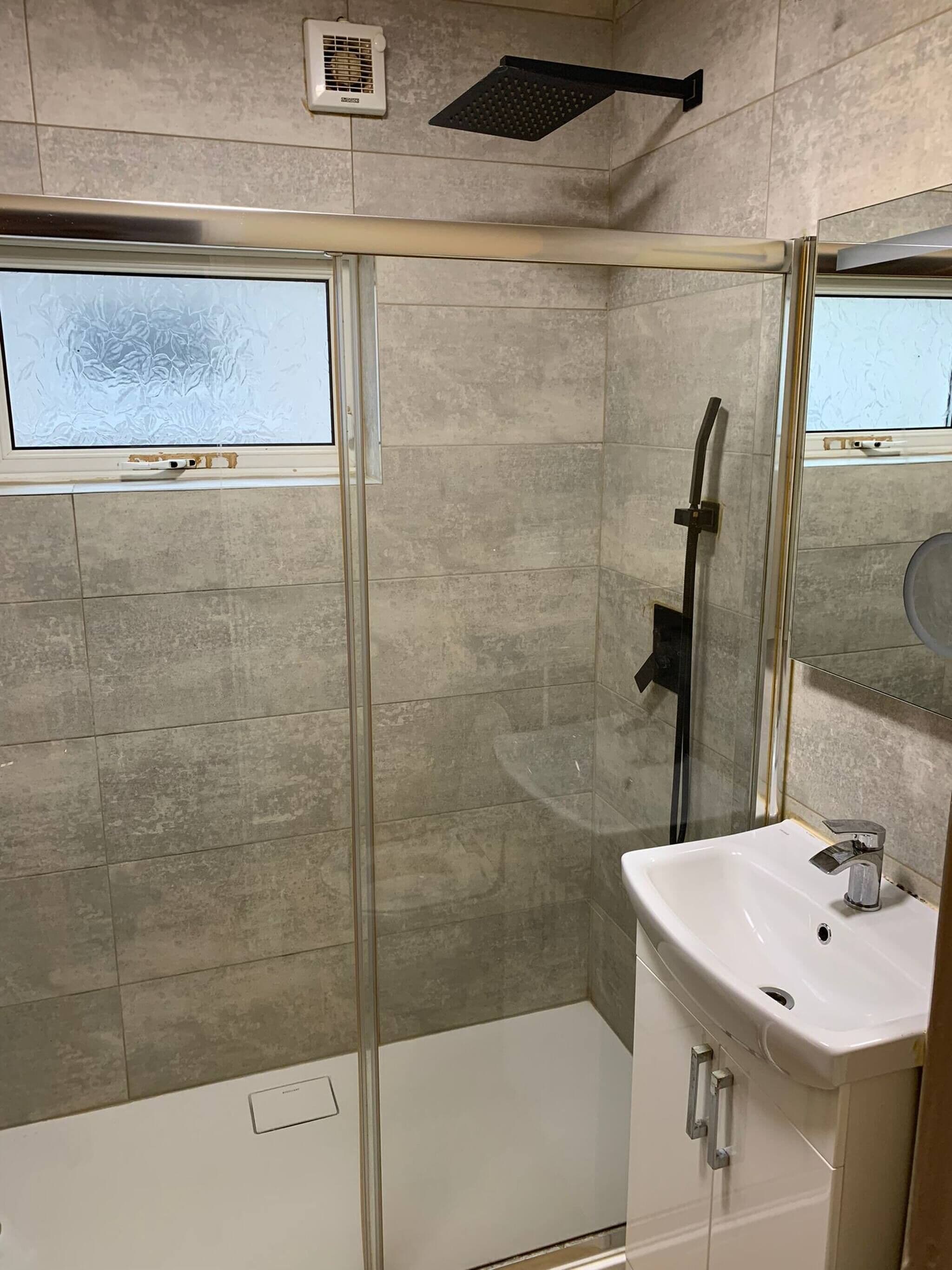 Un baño moderno con ducha de vidrio, un lavamanos blanco y un espejo encima.