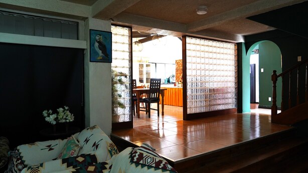 Una sala de estar con un sofá, una zona de comedor con una mesa y sillas, y una cocina visible a través de un mamparo de vidrio.