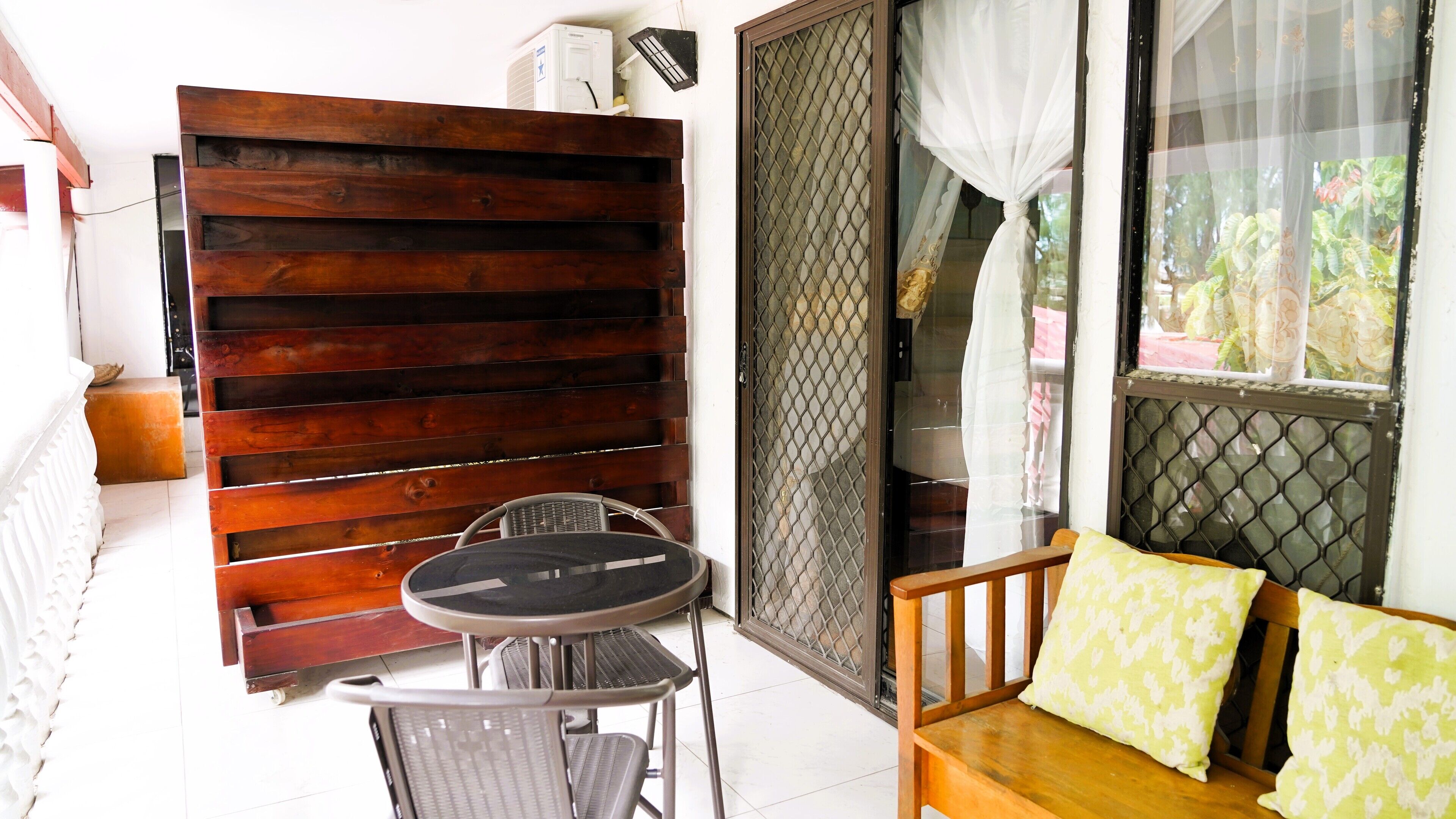 A balcony with a wooden partition, a table with two chairs, and a sofa with cushions.