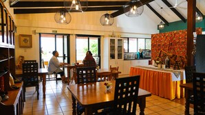 Un restaurante acogedor con mesas y sillas de madera, una zona de cocina y lámparas colgantes.