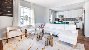 A modern living room with a glass coffee table, white sofas, and a kitchen in the background. - 3BR Prime Luxury near NYC w Arcade Room (Yonkers)
