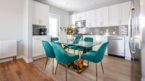 A modern kitchen with white cabinets, a glass dining table, teal chairs, and stainless steel appliances. - 3BR Prime Luxury near NYC w Arcade Room (Yonkers)
