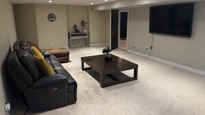 A living room with a black leather sofa, a coffee table, a TV, and a door leading to another room. - Charming 2 bedroom bed & breakfast in fabulous Niagara-on-the-Lake with pool (Niagara-on-the-Lake)