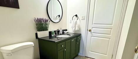 A bathroom with a toilet, sink, and mirror. There is a door to the right and a painting on the wall.