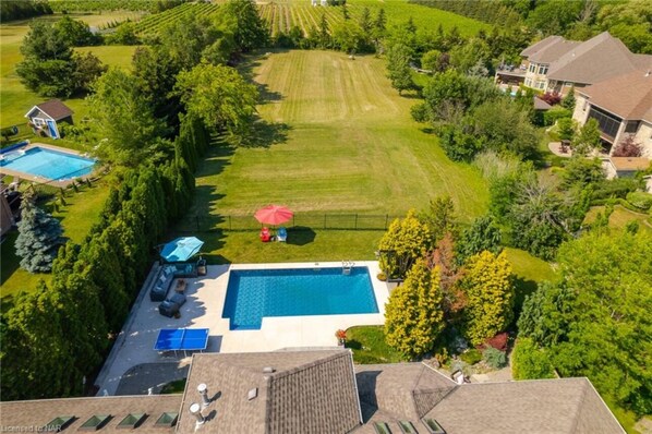 Vista aérea de una propiedad residencial con piscina, cancha de tenis y césped bien cuidado.