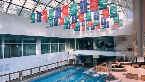 Une piscine intérieure avec des couloirs bien délimités, entourée d’une verrière et agrémentée de diverses banderoles.
