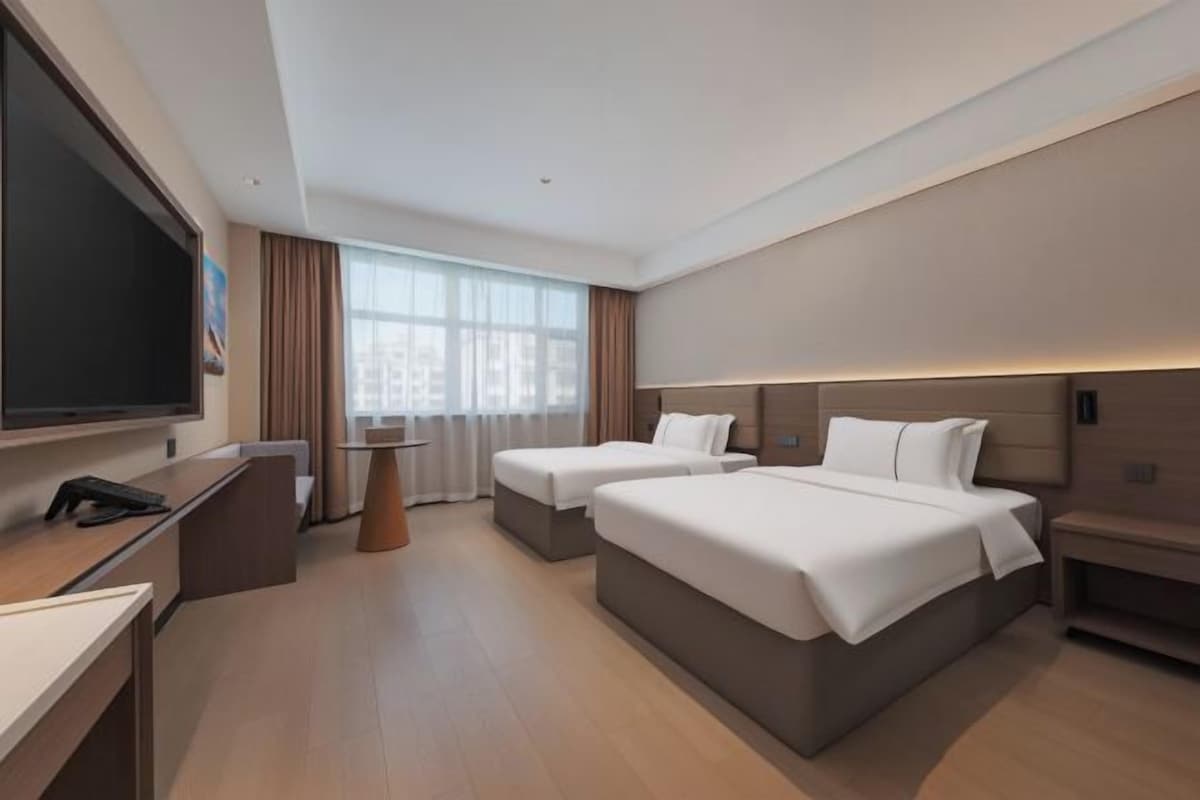 A hotel room with two beds, a desk, a TV, and a window with curtains.