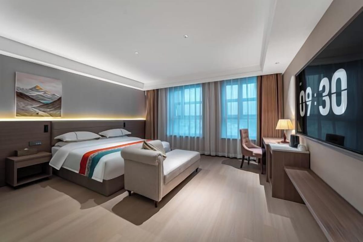 Una habitación de hotel moderna con cama, mesita de noche, escritorio, silla y un ventanal grande.