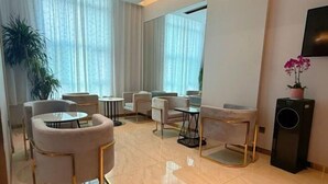 Une chambre d’hôtel moderne dotée d’un coin salon avec des tables rondes et des fauteuils confortables, d’un grand miroir et d’une orchidée en pot.