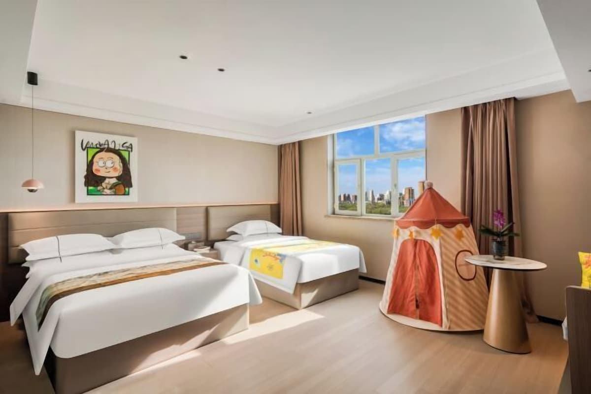 Habitación de hotel con dos camas, una ventana con vista a la ciudad, una estructura parecida a una tienda de campaña y una mesita con un florero.