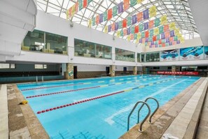 An indoor swimming pool with multiple lanes, glass walls, and a high ceiling with colorful banners. - Shangdong Lake Hotel (Kuytun)