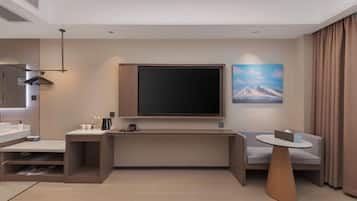 Et moderne hotelværelse med fjernsyn, sofa, sofabord, skrivebord og stort vindue.