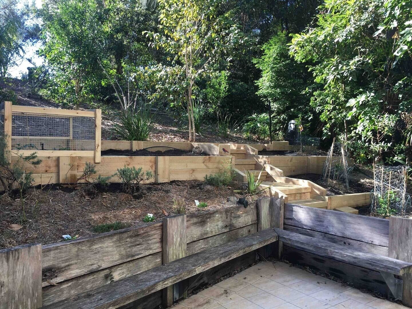Un jardín con jardineras elevadas de madera, un banco de madera y un cartel.