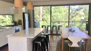 A modern kitchen with a large island, white cabinets, and a dining area with a wooden table and white chairs. - Private, Secluded Retreat - Our Reviews Say it All (Smiths Lake)