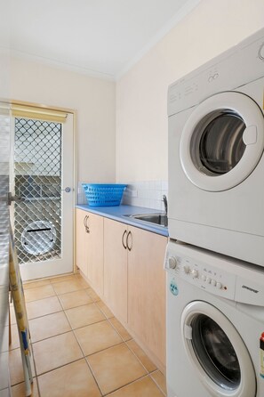 Een wasruimte met een voorlader wasmachine en droger, een blauwe wasmand en een betegelde vloer.