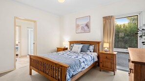 Une chambre à coucher avec un lit en bois, des tables de chevet, une commode, une fenêtre avec des rideaux et un tableau accroché au mur.