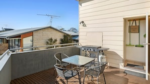 A balcony with a table and chairs, a barbecue grill, and a door with a bag hanging on it. - Family Tides (Apollo Bay)